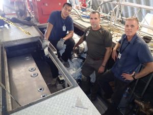 Manny Beltran, Glen Adams, and Tim McIntosh standing below deck after lowering one of the portside fuel tanks into the engine room.