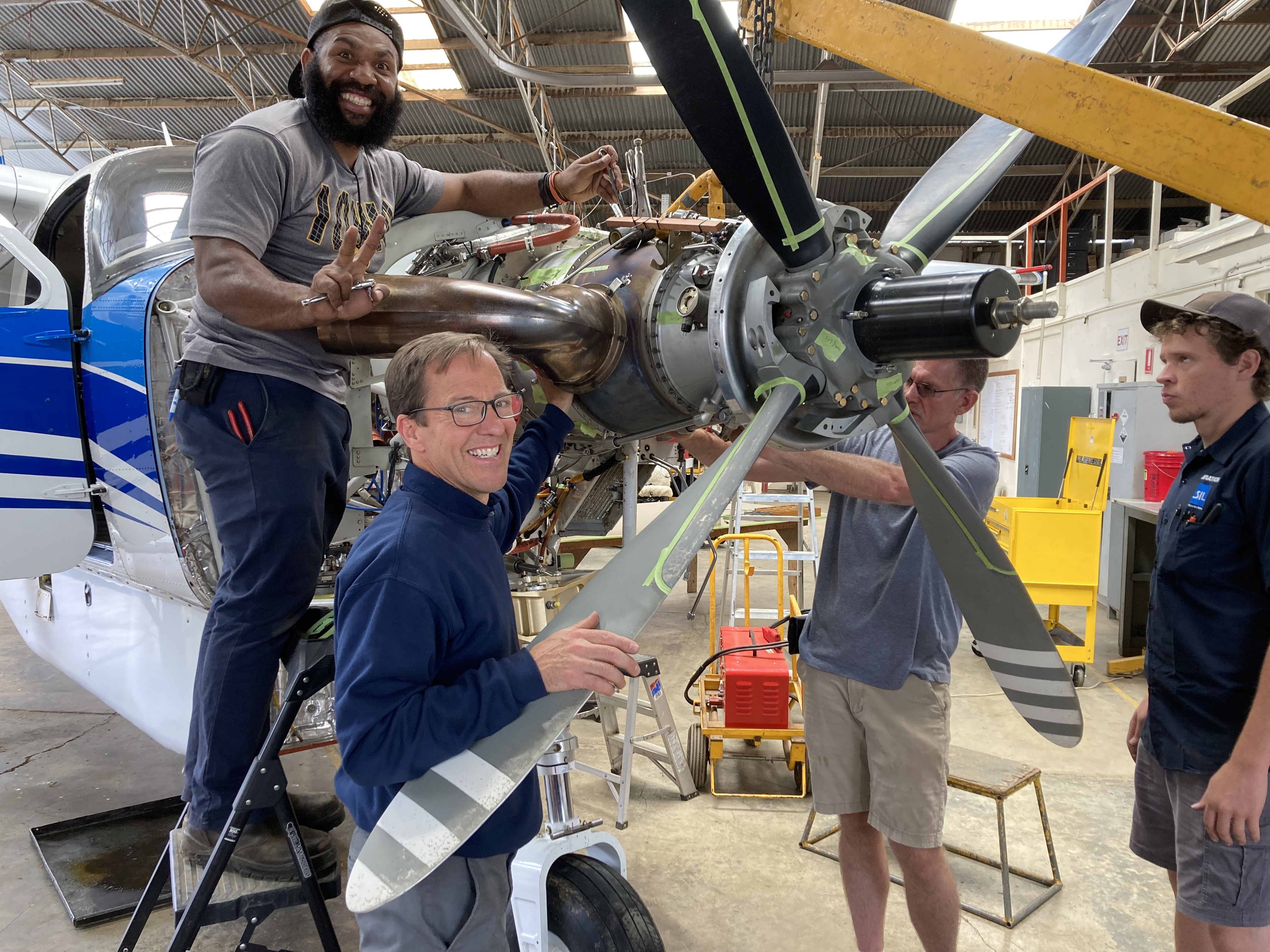 Four men work on an engine in a hangar