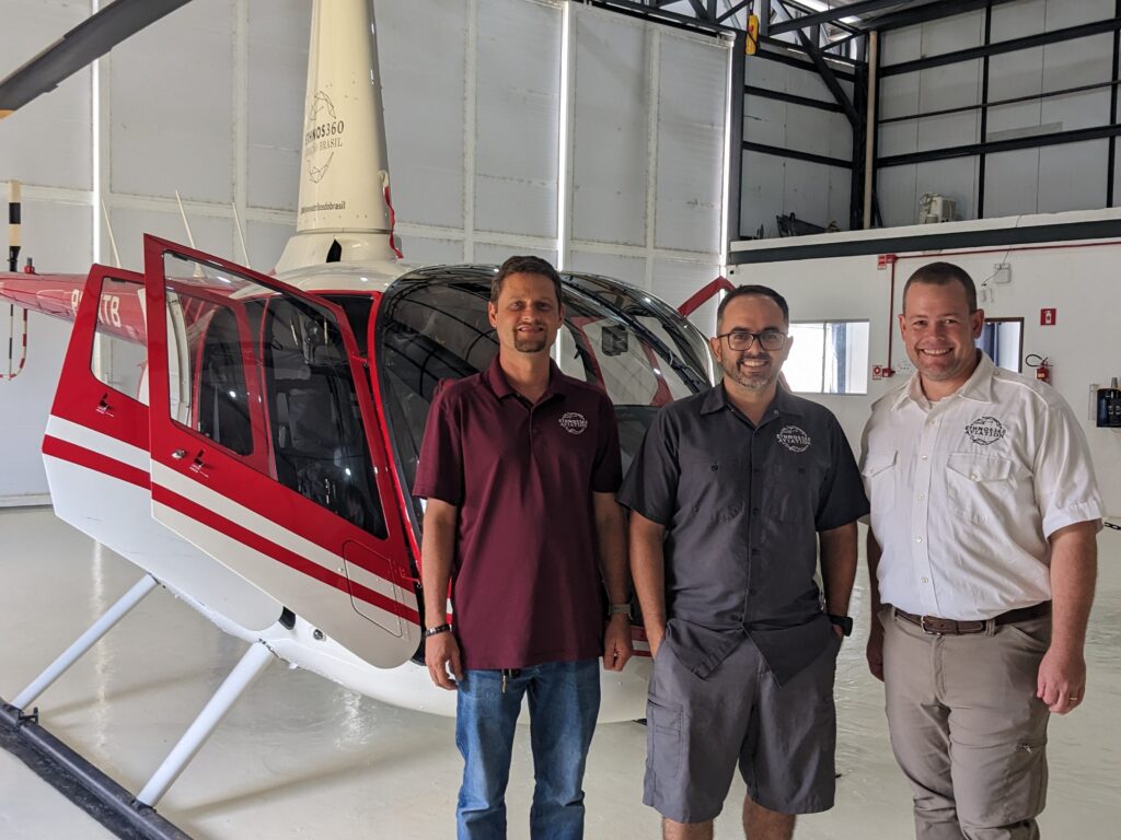 Three helicopter pilots stand in front of a R66 helicopter in a hangar in Brazil