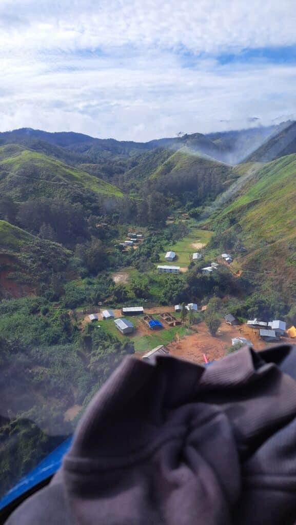 Looking out of a helicopter window into a town in a ravine in Papua New Guinea.