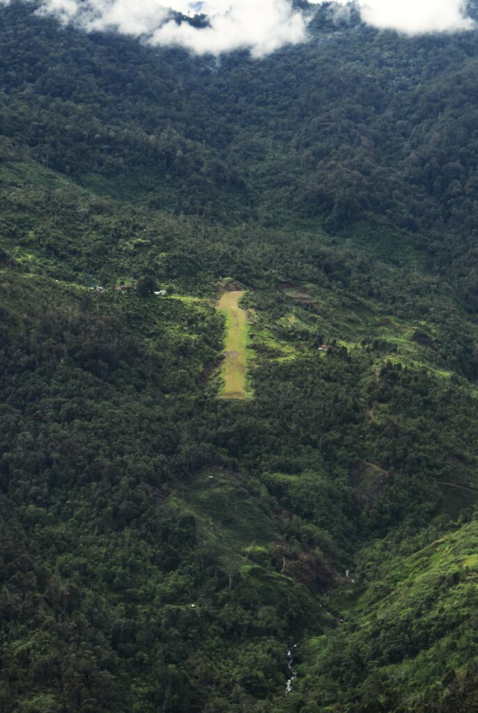 A grass airstrip in Indonesia surrounded by mountains ensconced in jungle.