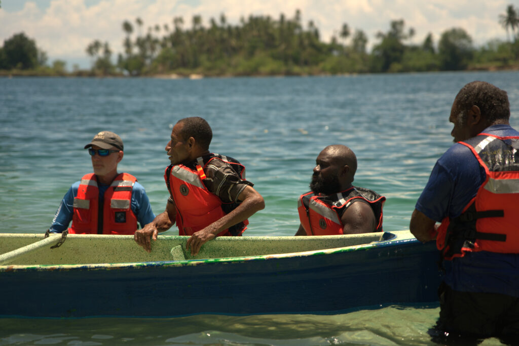 A group of men in life jackets-one American and three Papua New Guineans-stand beside a dinghy in the water in Papua New Guinea.