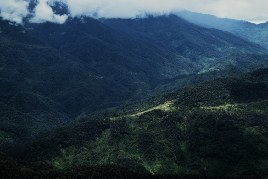 A far-away shot of a grass aistrip on top of a mountain surrounded by other mountains in Papua, Indonesia
